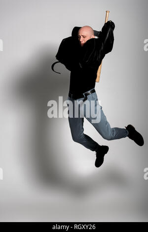 Homme chauve agressif en blouson de cuir holding baseball bat et sautant sur gris Banque D'Images