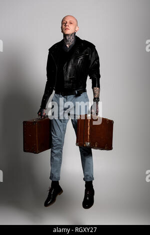 Sur toute la longueur de handsome tattooed man en blouson de cuir valises holding et de sauter sur gray Banque D'Images