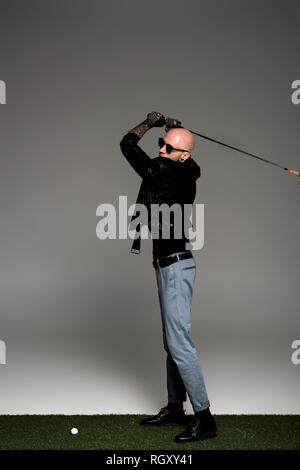 Sur toute la longueur de l'homme tatoué en blouson de cuir et lunettes de soleil en jouant au golf sur gris Banque D'Images