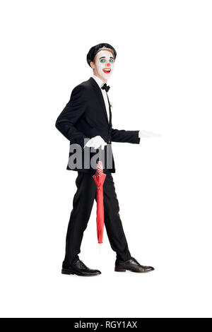 Clown joyeux en costume et béret noir holding umbrella en marchant isolated on white Banque D'Images