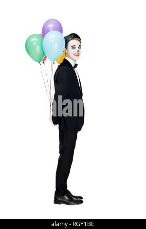 Clown joyeux en costume et béret noir holding ballons d'hélium derrière retour isolated on white Banque D'Images