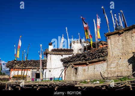 Façades de maisons traditionnelles du village, du bois stocké sur les toits, les drapeaux de prières bouddhistes colorés voletant dans l'air Banque D'Images