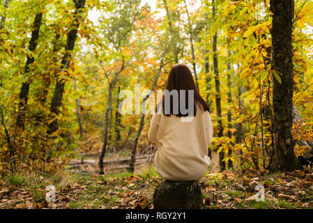 Une jeune femme aux cheveux roux assis sur son dos sur une pierre dans une forêt d'automne Banque D'Images