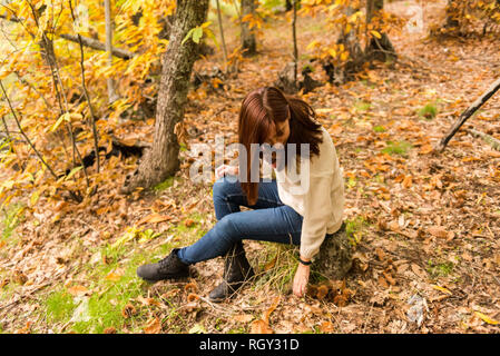 Femme aux cheveux roux assis sur une pierre recueille des châtaignes du sol dans une forêt d'automne Banque D'Images