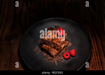 Les framboises et deux brownies sur une plaque noire avec des copeaux de chocolat sur la table en bois sombre. Format horizontal avec l'exemplaire de l'espace. Banque D'Images