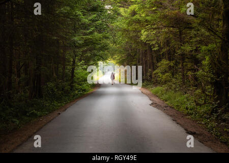 Femme marche sur la pittoresque route forestière pendant une journée d'été. Prises à Florencia Bay, près de l'Ucluelet et Tofino, Vancouver Island, BC, Canada. Banque D'Images