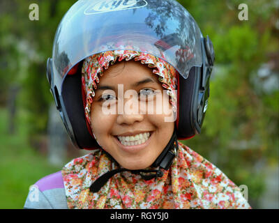 Jeune femme indonésienne de Kalimantan porte un casque de moto moderne sur son hijab traditionnel et sourit pour la photo. Banque D'Images