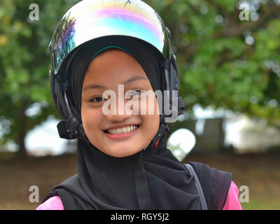 Souriant, jolie fille Malais musulmans porte un casque de moto moderne sur son hijab traditionnel noir. Banque D'Images