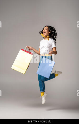 Beautiful young asian woman jumping avec sourire heureux tout en maintenant des sacs colorés sur gris Banque D'Images