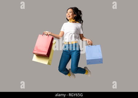 Rire asian woman holding shopping bags colorés et heureusement isolés saut sur gris Banque D'Images