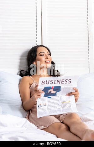 Young Asian Woman Reading journal d'affaires tout en restant au lit Banque D'Images