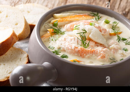 Gros plan du crème scandinave de la soupe de poisson avec la morue, le saumon et les légumes dans un bol servi avec du pain frais sur la table horizontale. Banque D'Images