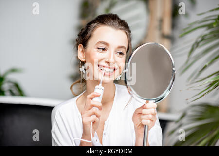 Belle femme nettoyer les dents avec l'outil de recherche dans l'irrigator miroir dans la salle de bains Banque D'Images