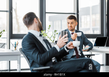 Portrait of businessman holding cup avec boisson et assis près de collègue Banque D'Images