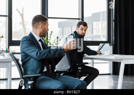 Portrait of businessman holding laptop et assis près de collègue Banque D'Images