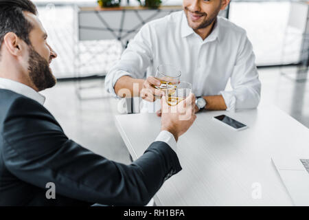 Homme barbu toasting with whiskey tout en restant assis dans un bureau moderne avec un collègue Banque D'Images