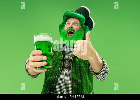 A smiling happy senior man in a leprechaun chapeau avec la bière verte au studio. Il célèbre le Jour de la Saint Patrick. La célébration, à la fête, la bière, maison de vacances, d'alcool, party concept Banque D'Images