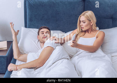 Choqué woman smartphone pour confondre copain au lit, la méfiance à l'idée Banque D'Images