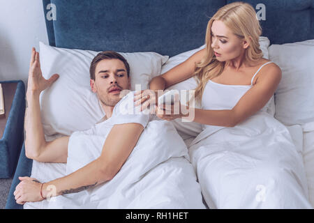High angle view of young woman showing smartphone pour confondre boyfriend Lying in Bed Banque D'Images