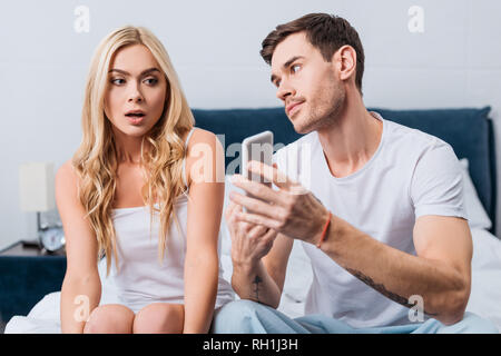 L'homme jaloux montrant smartphone pour confondre amie assis sur le lit, la méfiance concept Banque D'Images