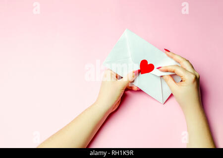La main féminine s'ouvre l'enveloppe avec un cœur rouge. Une lettre d'amour à l'être aimé. Valentines Day concept. Carte de voeux saint valentin. Déclaration d'amour. Weddi Banque D'Images