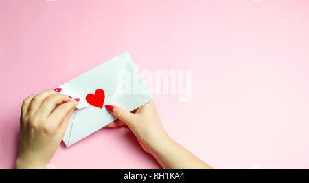 La main féminine s'ouvre l'enveloppe avec un cœur rouge. Une lettre d'amour à l'être aimé. Valentines Day concept. Carte de voeux saint valentin. Déclaration d'amour. Weddi Banque D'Images
