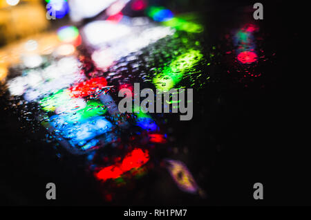 Reflets colorés et de gouttes de pluie sur un capot de voiture noire humide. Résumé nuit ville arrière-plan flou Banque D'Images