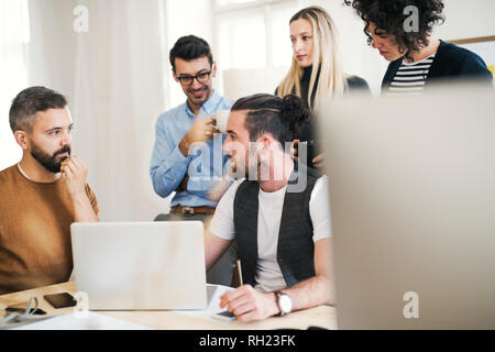 Groupe de jeunes hommes et femmes concentré d'affaires avec ordinateur portable ayant une réunion dans un bureau moderne. Banque D'Images