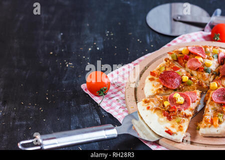 Pizza avec du maïs, des saucisses, des tomates rondes en bois sur le bord Banque D'Images