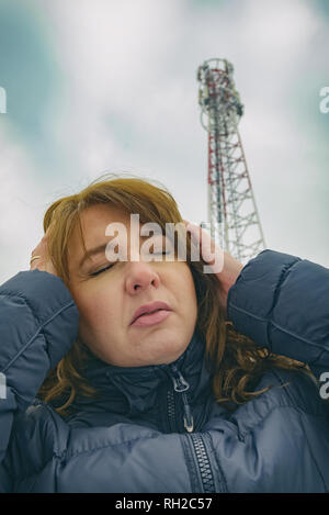 La femme tient sa tête près de la BTS. Rayonnement nocif par le réseau de téléphonie mobile concept transmetteurs Banque D'Images