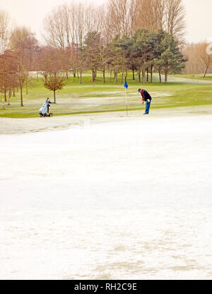 L'homme jouant le golf en hiver sur un cours de golf en dépit de la neige et des températures glaciales à Malkins Bank près de Sandbach Cheshire England UK Banque D'Images