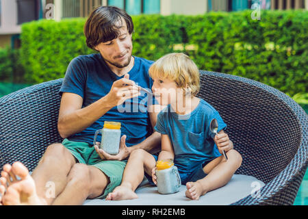 Père et fils manger le dessert avec chia seeds et de mangues à la piscine le matin. la saine alimentation, l'alimentation, les régimes végétariens et personnes concept Banque D'Images
