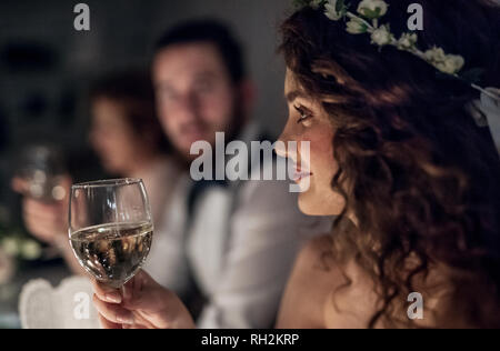 Un gros plan d'une jeune femme assise à une table sur un mariage, tenant un verre de vin blanc. Banque D'Images