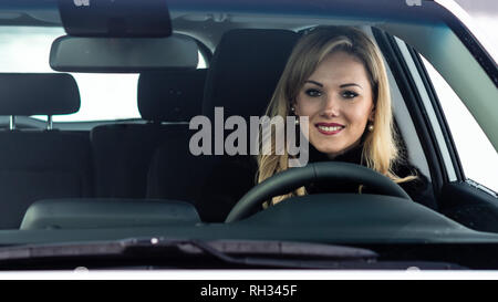 Femme blonde est assis à une voiture blanche direction et vu à travers la fenêtre. Banque D'Images