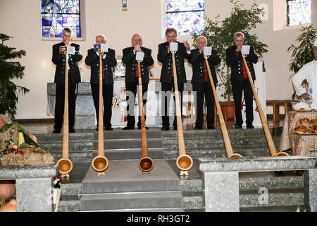 Six hommes en tenues traditionnelles jouent l'Alpenhorn dans l'église locale pour Thanksgiving à Sasbach, Allemagne, Forêt Noire. Banque D'Images