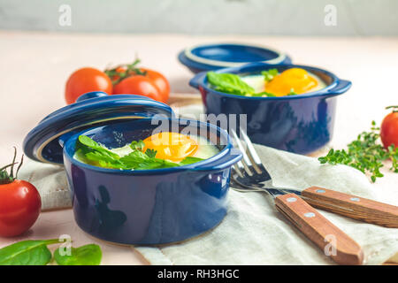 Oeufs cocotte kokot petit-déjeuner français. Oeufs cuits en bleu moules de cuisson en céramique. Cocotte de légumes et portionné oeufs dans le style italien. Banque D'Images