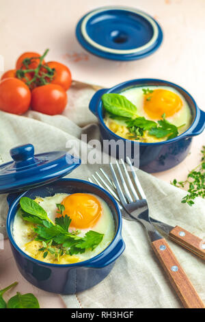 Oeufs cocotte kokot petit-déjeuner français. Oeufs cuits en bleu moules de cuisson en céramique. Cocotte de légumes et portionné oeufs dans le style italien. Banque D'Images