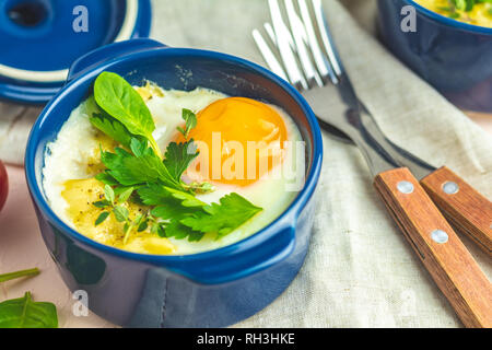Oeufs cocotte kokot petit-déjeuner français. Oeufs cuits en bleu moules de cuisson en céramique. Cocotte de légumes et portionné oeufs dans le style italien. Banque D'Images