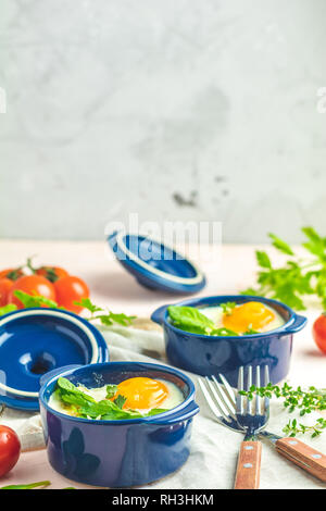 Oeufs cocotte kokot petit-déjeuner français. Oeufs cuits en bleu moules de cuisson en céramique. Cocotte de légumes et portionné oeufs dans le style italien. Banque D'Images