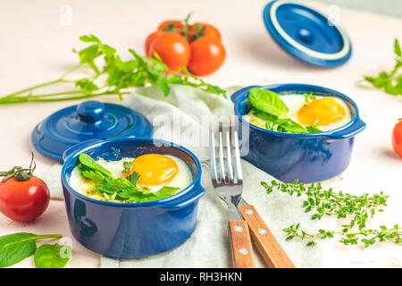 Oeufs cocotte kokot petit-déjeuner français. Oeufs cuits en bleu moules de cuisson en céramique. Cocotte de légumes et portionné oeufs dans le style italien. Banque D'Images