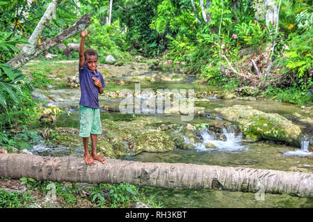 Ni-Van Boy Standing on Log en rivière. Banque D'Images