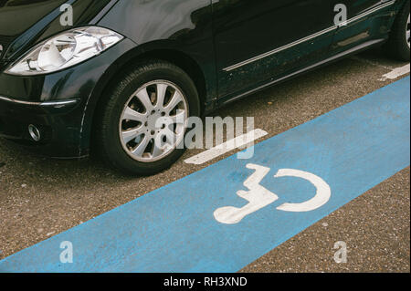 Détail de voiture près de bande bleue dédiée aux personnes à mobilité réduite Parkings avec pictogramme blanc peint sur un asphalte Banque D'Images