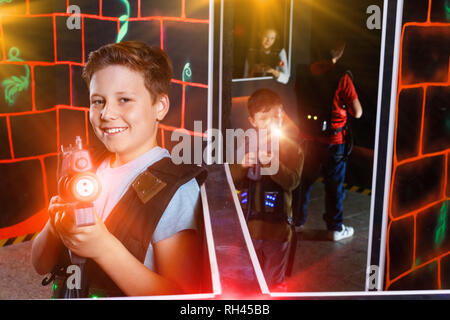 Portrait of smiling preteen boy amical positif avec pistolet laser posant en labyrinthe laser tag Banque D'Images