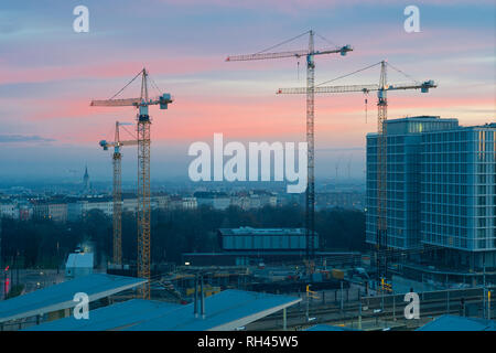 Quatre grues de construction in early morning light avec les toits de Vienne avec un ciel dramatique avec orange, bleu et rose teintes. Banque D'Images