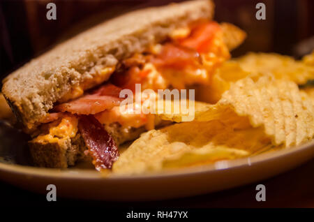 Un style sud-pimiento cheese sandwich est servi sur pain de blé entier, accentués avec du bacon et des tranches de tomates, et servi avec des croustilles de pommes de terre. Banque D'Images