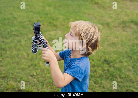 Petit garçon tire une vidéo sur un appareil photo d'action sur un fond d'herbe verte Banque D'Images