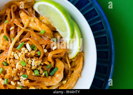 Les nouilles pad Thaï au poulet, l'arachide, l'oignon vert, et de la chaux sur les plaques bleu et blanc et coloré de la surface verte. Banque D'Images