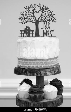 Gâteau de mariage et cupcakes au chocolat à la vanille servis comme dessert lors d'une réception à thème rustique image noir et blanc Banque D'Images