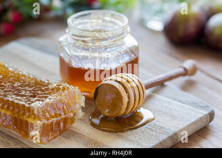 Et du miel d'abeilles collante jar sur planche de bois avec des figues et des baies. Banque D'Images