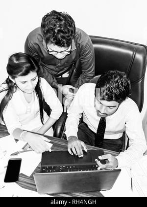 Équipe de deux jeunes hommes et une femme indienne dans l'office, au bureau avec ordinateur portable, des graphiques sur des feuilles c220300 smartphone. Image en noir et blanc Banque D'Images